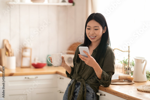 Happy korean woman checking messages while drinking coffee