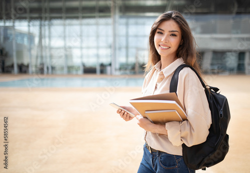 Happy young european woman student in casual with backpack, books and smartphone go to study