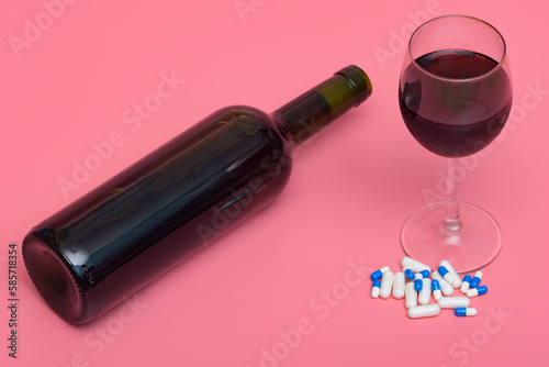 Przewrócona butelka wina obok napełnionego kieliszka i tabletek