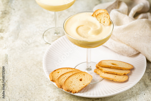 Zabaione or sabayon, or advocaat in a champagne coupe, alcoholic creamy drink or dessert. Cream made with egg yolks, sugar, and a sweet wine Marsala or liqueur. Baicoli biscuits. 