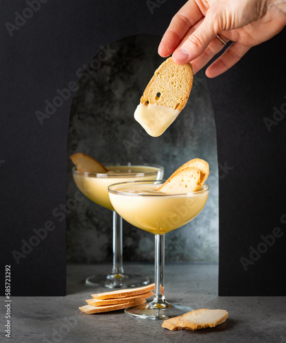 Eating Baicoli biscuit and zabaione zabaglione or sabayon in a champagne coupe. Italian cream-based dessert, made with egg yolks, sugar, and a sweet wine Marsala Light custard, whipped cream.