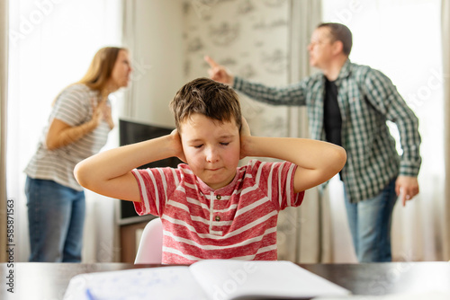 Sad child covers his ears with his hands during an argument between his parents