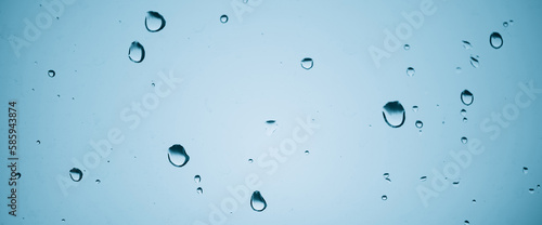 Minimal light backdrop with rain droplets on white glass. Light wet window with rainy drops closeup in blue light. Blurry minimalist monochrome background of window glass with raindrops close up.