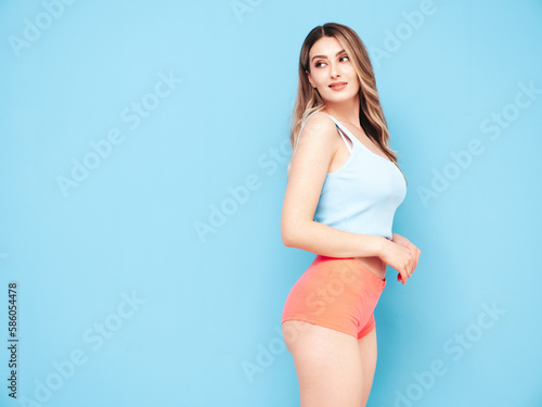 Portrait of young beautiful smiling female in trendy summer shorts clothes. Carefree woman posing near blue wall in studio. Sexy positive model having fun indoors. Cheerful and happy