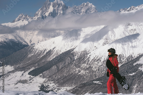 Snowboarder female out of focus walking with snowboard in beautiful mountains tops covered with snow and clouds on background