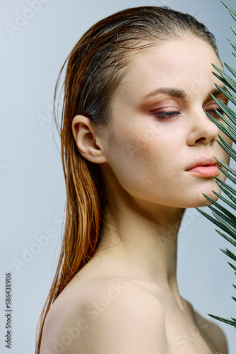 a close beauty portrait of a beautiful woman standing holding a palm leaf near her face, closing her eyes. Vertical photo without retouching of problem skin