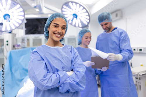 Close-up of a surgeon woman looking at camera with colleagues performing in background in operation room. The concept of medicine