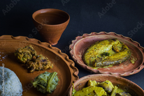 Traditional Bengali indian meal served on clay plate consisting of boiled rice, shukto, fish curry, leafy greens mixed with mashed potato etc, maintaining local bengali culture.