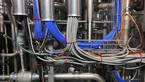 A bundle of grey, blue, and orange cable among pipes in production room of factory