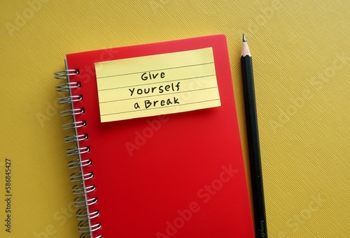 Note stick on red notebook with handwritten text GIVE YOURSELF A BREAK, concept of self compassion - self reminder to treat yourself as you would a friend with kindness and understanding
