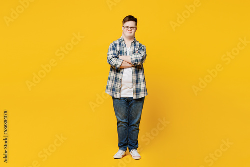 Full body young smiling man with down syndrome wears glasses casual clothes look camera hold hands crossed folded isolated on pastel plain yellow color background. Genetic disease world day concept.