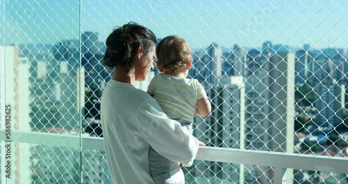 Mom holding baby looking at city view from apartment balcony with safety net
