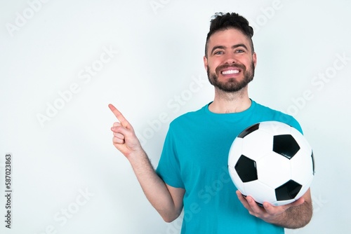 Young man holding a ball over white background looking at camera indicating finger empty space sales