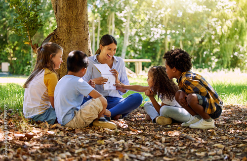 Books, reading or teacher with children in a park storytelling for learning development or growth. Smile, tree or happy educator with stories for education at a kids kindergarten school in nature