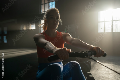Young athlete woman doing rowing exercises in dark concept gym