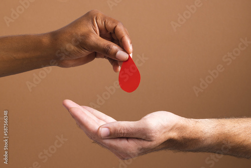 Hands of biracial man giving blood drop to caucasian man, on brown background