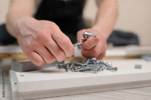 Furniture assembler takes a screw, a hex key in his hand, close-up. Self-assembly of furniture. The concept of moving, repairing, assembling furniture
