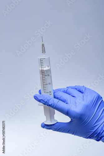 Duża biała strzykawka z igłą trzymana w dłoni w niebieskich rękawiczkach medycznych