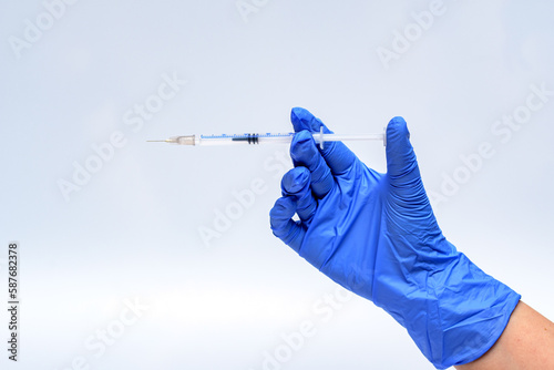 Strzykawka z igłą trzymana w dłoni w niebieskiej rękawiczce przez pielęgniarkę w przychodni