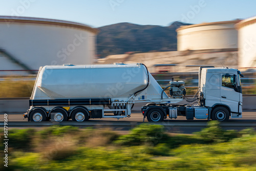 Tank truck for bulk cement transport circulating on a road, side view, sweeping effect.