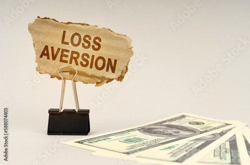 There is money on the table, next to it is a cardboard sign with the inscription - Loss Aversion