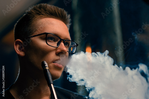 A man in glasses smokes a traditional hookah pipe A man exhales thick smoke in a hookah cafe or lounge bar