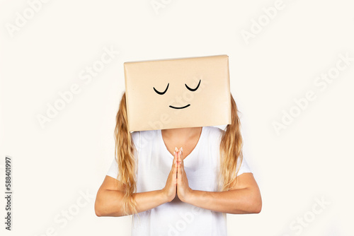 Mujer con caja de cartón en la cabeza con gesto de agradecimiento y con las manos juntas sobre un fondo blanco liso y aislado. Vista de frente y de cerca. Copy space