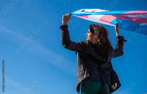 Transgender woman raising the trans flag in flight with a clear sky in the background. LGTBIQ+ activism