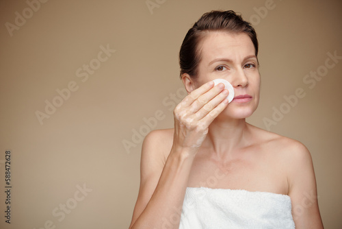 Mature woman wiping off make-up with cotton pad soaked in micelar water