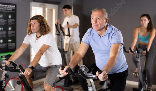 Positive mature male riding exercise bike during cycling class in modern gym
