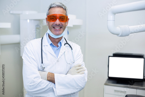 Portrait of smiling dentist standing with arms crossed