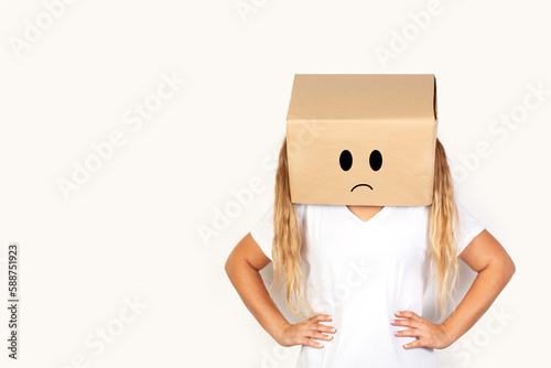 Mujer con caja de cartón en la cabeza y gesto de enfado y tristeza sobre un fondo blanco liso y aislado Vista de frente y de cerca. Copy space 