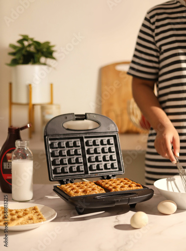 Waffle maker machine on kitchen marble floor. Waffles made by a girl.