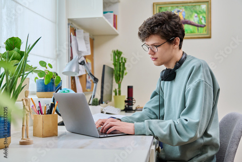 Young male college student sitting at desk at home using laptop