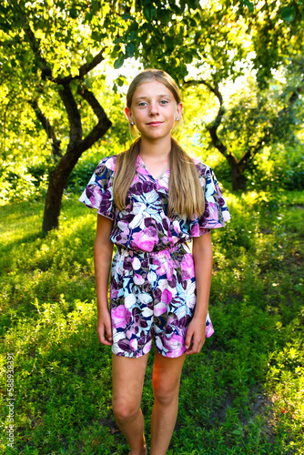 Summer teen girl. Defocus beautiful smiling teenage girl in dress standing against green summer background. High girl 12 or 13 years old on summer lawn. Vertical. Out of focus