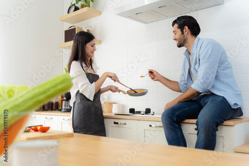 The man was tasting the food his girlfriend made for breakfast. A young couple in love having fun while preparing a breakfast together on a beautiful morning.