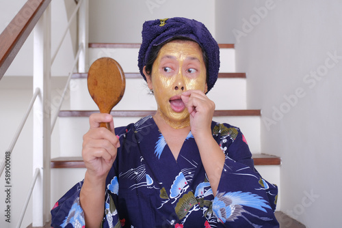 A woman looks at the mirror as she peels off her beauty mask; funny, silly expression.