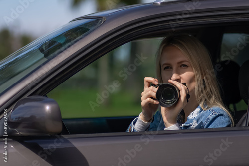 Woman with a camera sits in a car and takes pictures with a professional camera, a private detective or a paparazzi spy. Journalist is looking for sensations and follows celebrities.