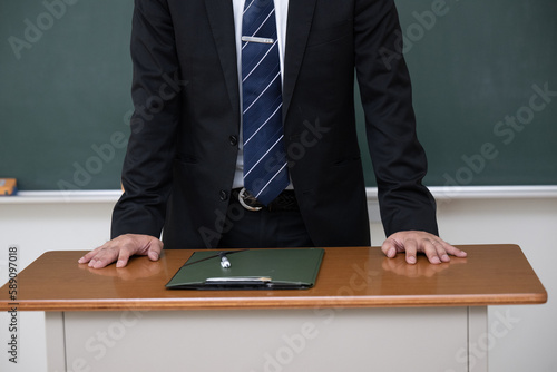 教壇の黒板の前に立つ男性教師の手元のアップ 