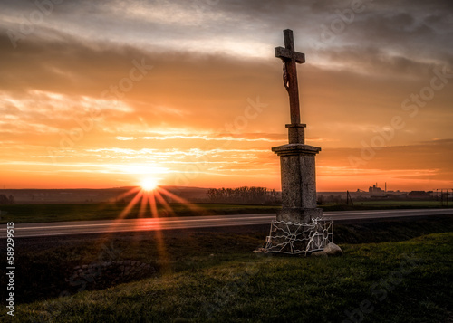 przydrożny krzyż i wschodzące słońce na czerwonym niebie