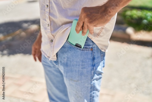 Young man holding smartphone to the pocket at street