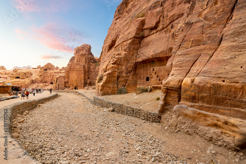 Tourists and visitors walk the canyon path through the Street of Facades alongside ancient Nabataean and Byzantine caves and tombs at the ancient Rose City of Petra, Jordan.