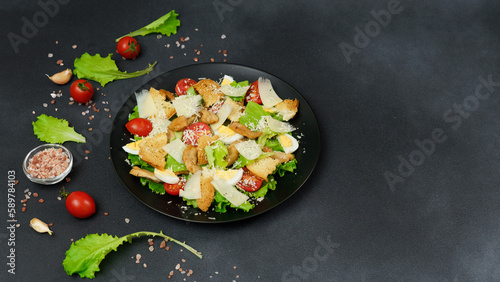 Top view of a Caesar Salad with chicken, lettuce leaves, cherry tomatoes, grated parmesan in a black plate against a Black Background