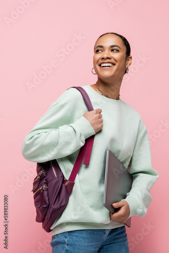 joyful african american student with backpack holding laptop isolated on pink.