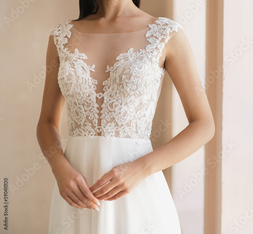 Front view of beautiful bride in the white wedding dress with deep neckline. Gorgeous sleeveless wedding dress decorated with lace