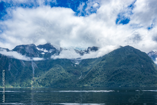 water falls and hanging glaciers seen from a boat in fjord with white clouds patagonia, aysen region, chile