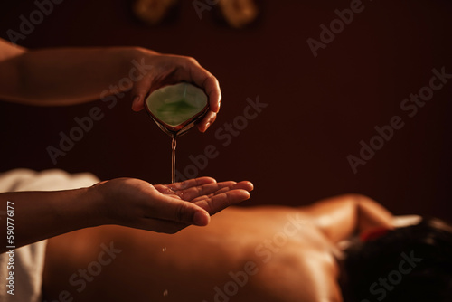 Masseur pouring aroma oil on hand, for massage on back of customer. Relaxation young male customer get service aromatherapy massage with masseuse in spa salon.