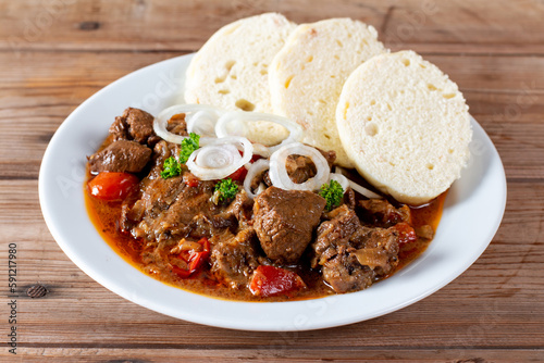 Czech traditional goulash with breaded dumpling and onion on white plate on table