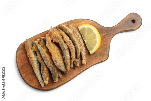 Wooden board with delicious fried anchovies and lemon on white background, top view