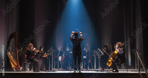 Cinematic Shot of an Orchestra on a Classic Theatre Stage: Professional Conductor Directing Symphony Orchestra with Performers Playing Violins, Cellos, and Trumpets During Music Concert